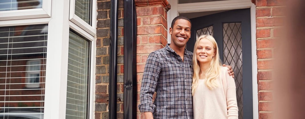 A young couple standing in front of a home