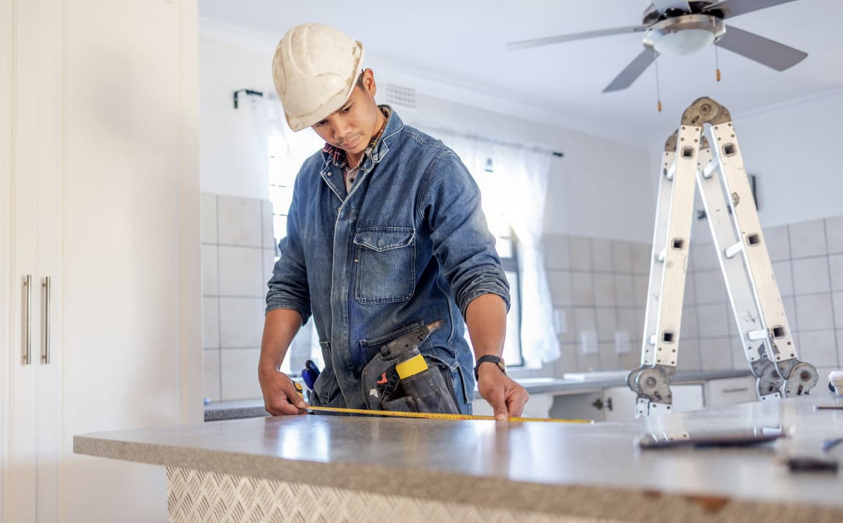 A contractor measuring a counter in a kitchen being renovated