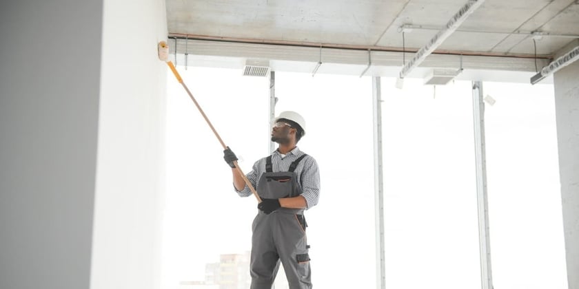A man painting the walls of a room white with a roller