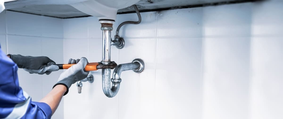 A plumber repairing a pipe under a sink, maintenance network concept
