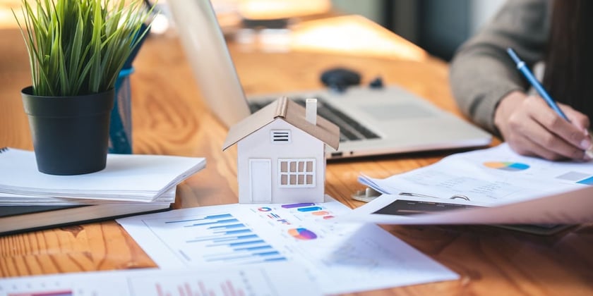 A small house next to papers with graphs and charts on them