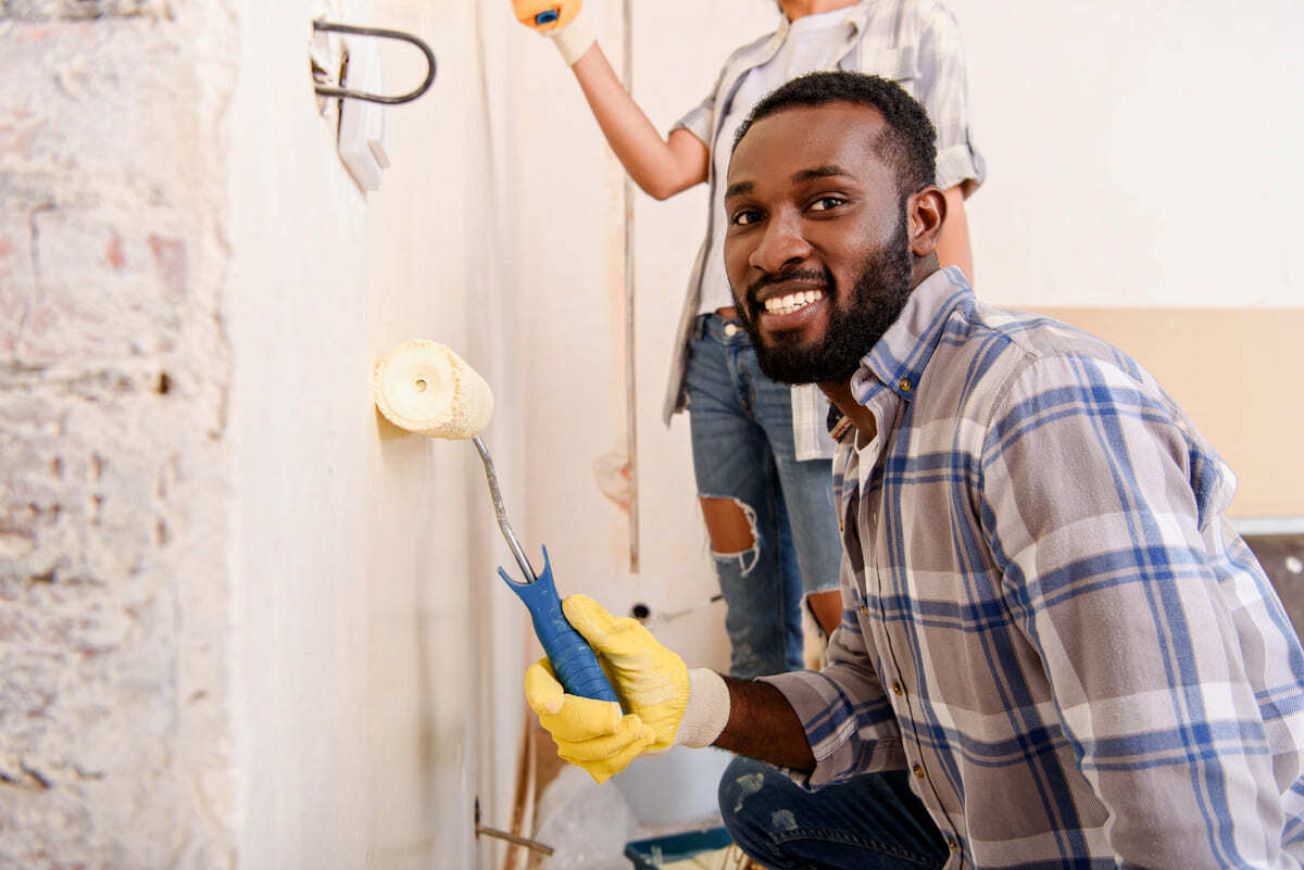 A smiling man painting a wall with a roller