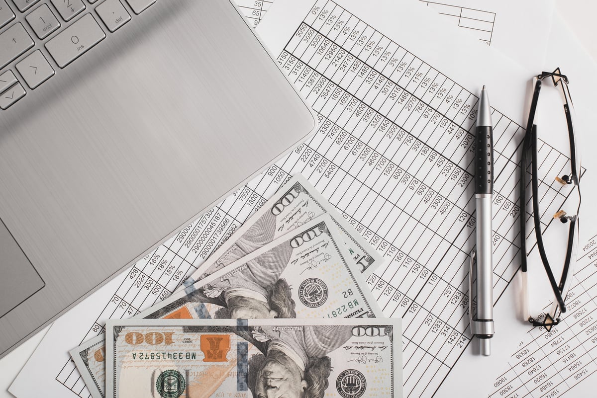 Cash next to a laptop and a spreadsheet