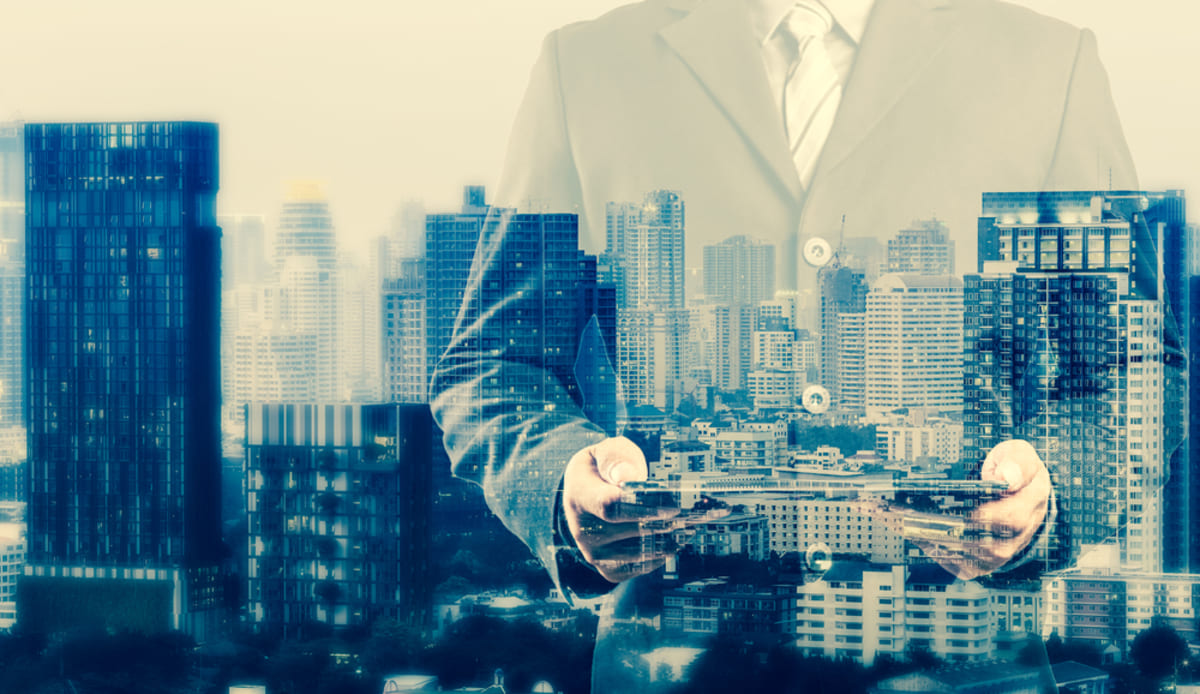Double exposure of successful property manager using digital tablet with city landscape background