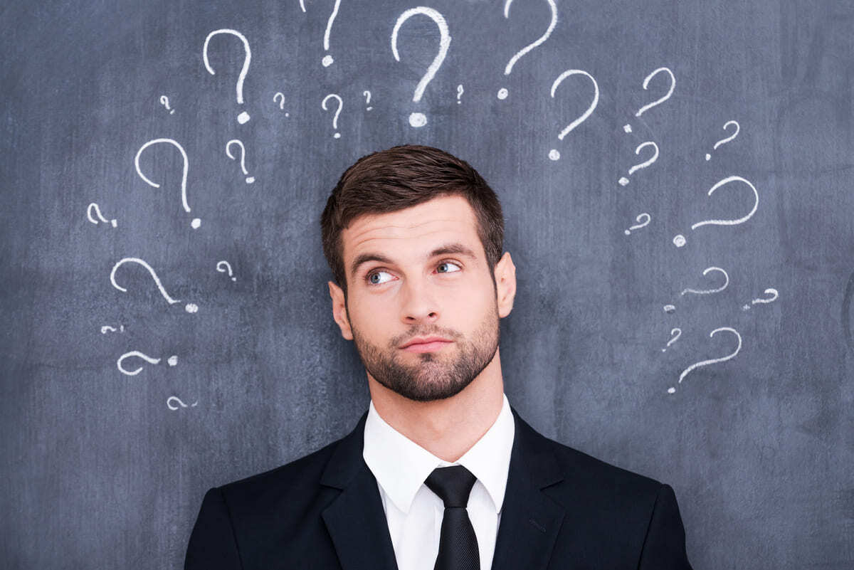Man confused standing in front of a blackboard with question marks