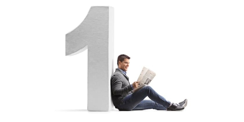 Young man reading a newspaper and leaning against a cardboard number one