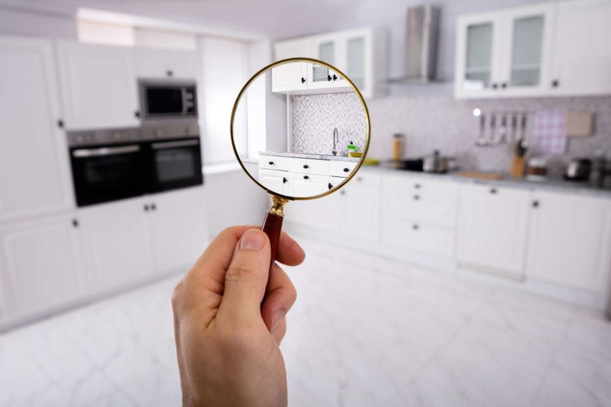 Close-up Of A Mans Hand Holding Magnifying Glass Over The Kitchen