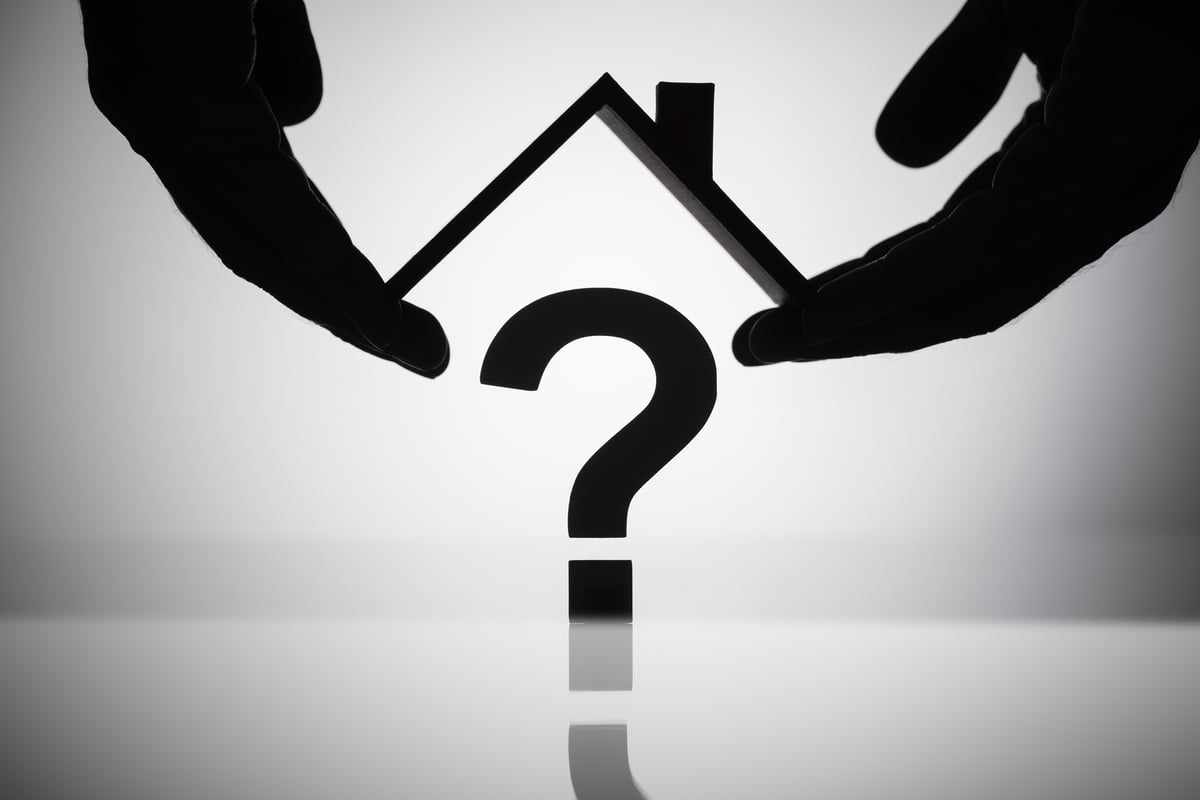 A Person's Hand Holding Roof Over Question Mark Sign, should i rent my home or sell it concept. 