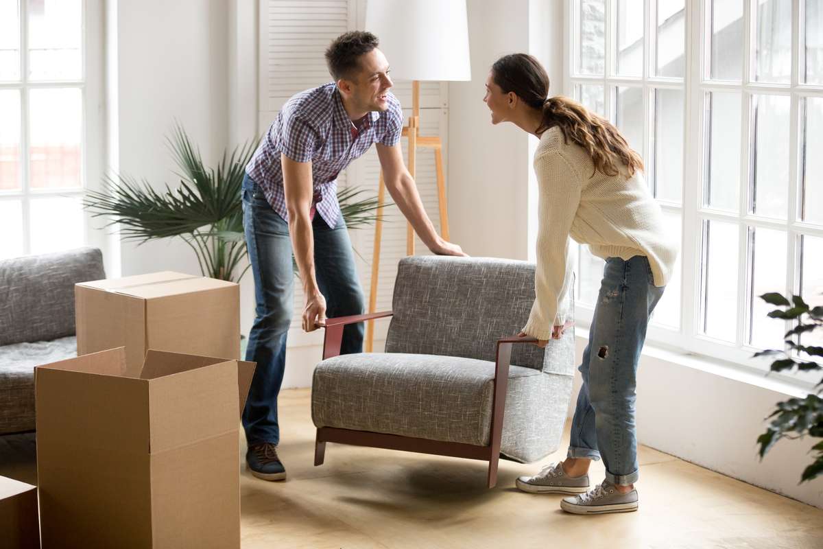 Couple carrying chair together, placing furniture moving in new (R) (S)