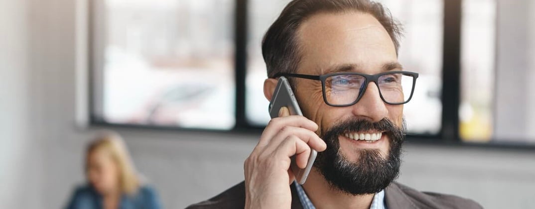 A bearded man on the phone smiling