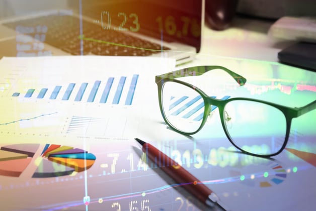 Laptop, graphs, and glasses on desk to exemplify real estate portfolio management.