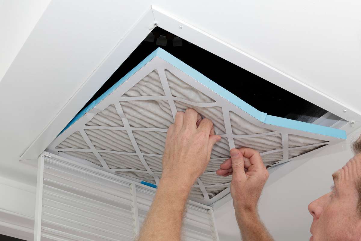 Person removing a dirty air filter from a ceiling intake vent, maintenance request concept. 