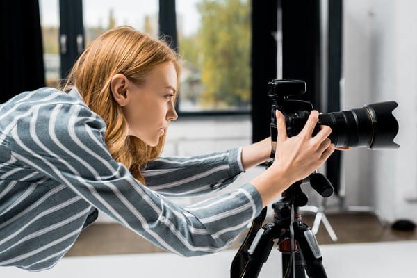 Side view of young female photographer working with professional photo camera in studio