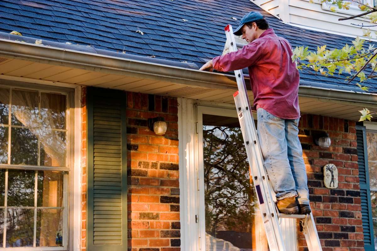 A man on a ladder cleaning gutters while maintaining a rental property