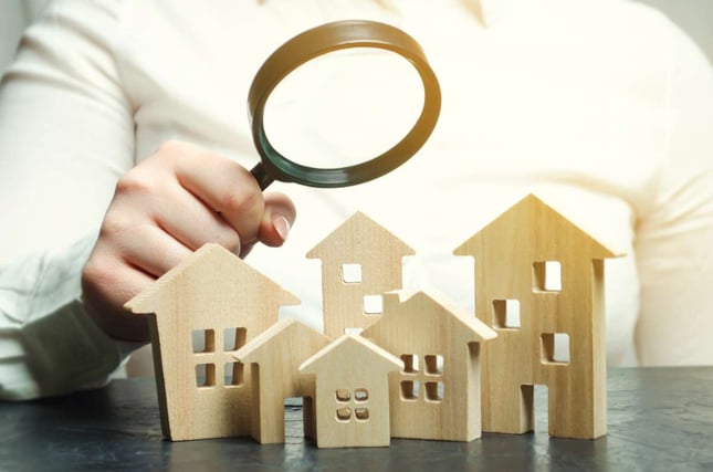 A woman is holding a magnifying glass over a wooden houses. Real estate appraiser. Find a house. Real estate market analysis