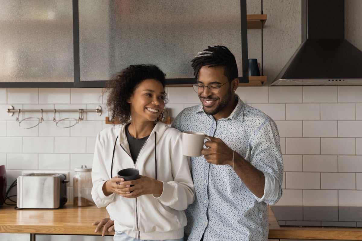 Affectionate millennial african american couple meet morning at cozy kitchen embracing talking enjoying hot drinks