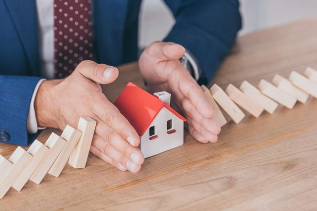 Cropped view of risk manager protecting house model from domino effect of falling wooden blocks with hands