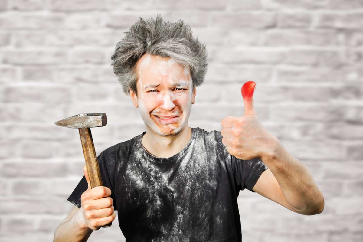 Dirty young builder guy fail is hold a hammer, hit the finger on brick wall background at home during repairs