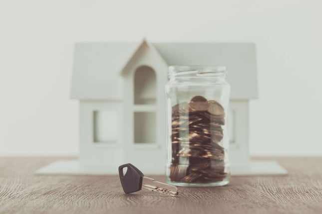 Key near jar of coins on table with small house on background, return on investment concept
