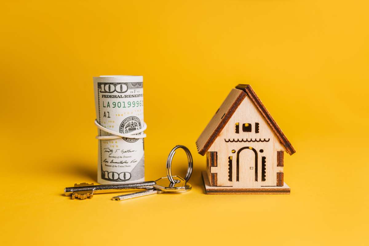 Miniature model of the house, keys and money on a yellow background