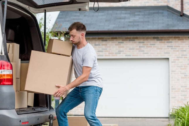 Strenuous young man moving boxes from car into new house