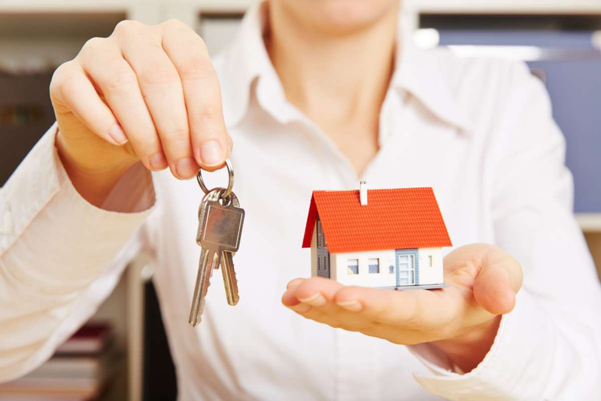 Womans hands holding two keys and a small house