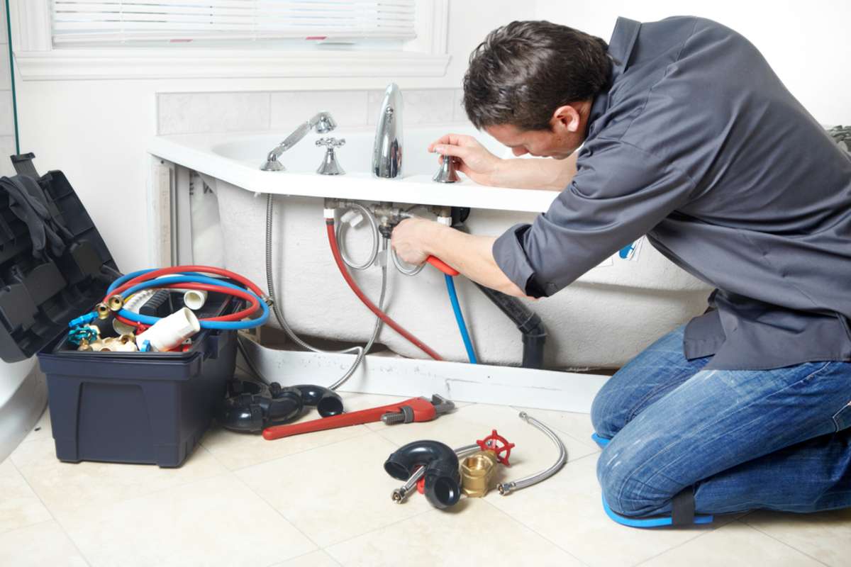 Young handsome plumber repearing bath tub. Service