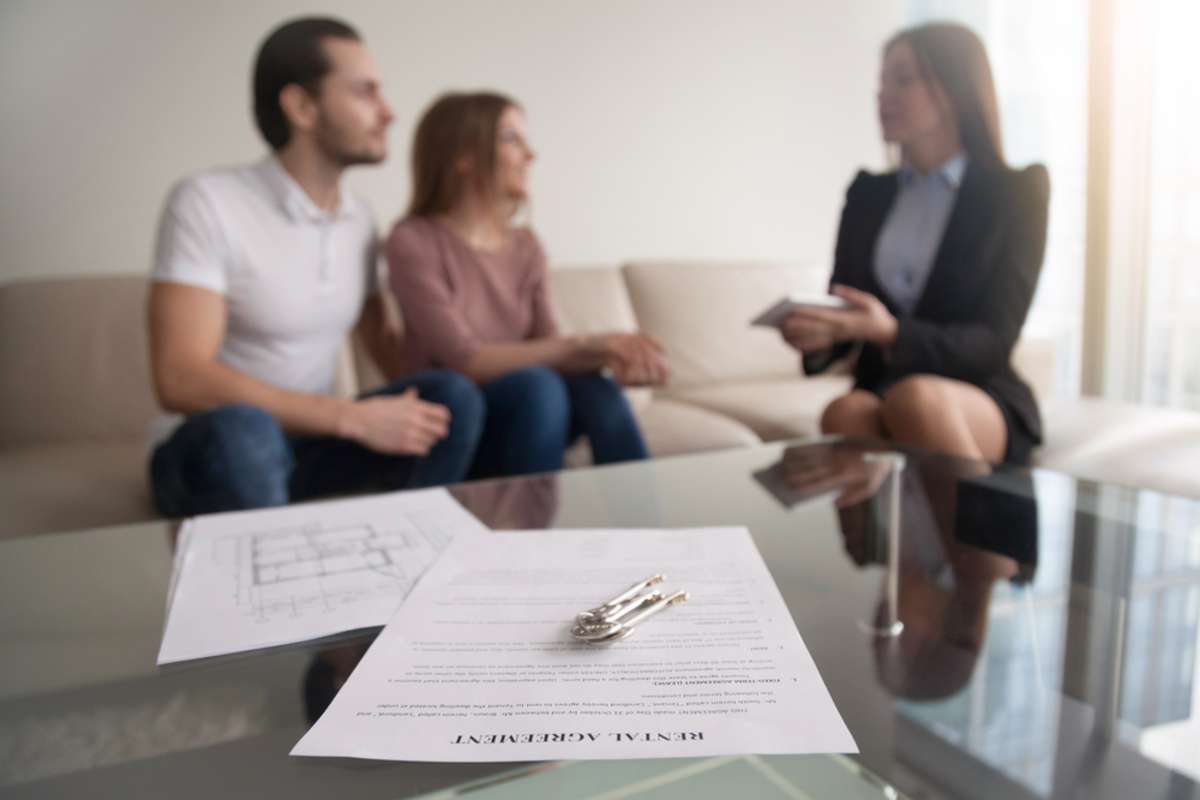 Young renters couple sitting on couch discussing renting apartment with real estate agent