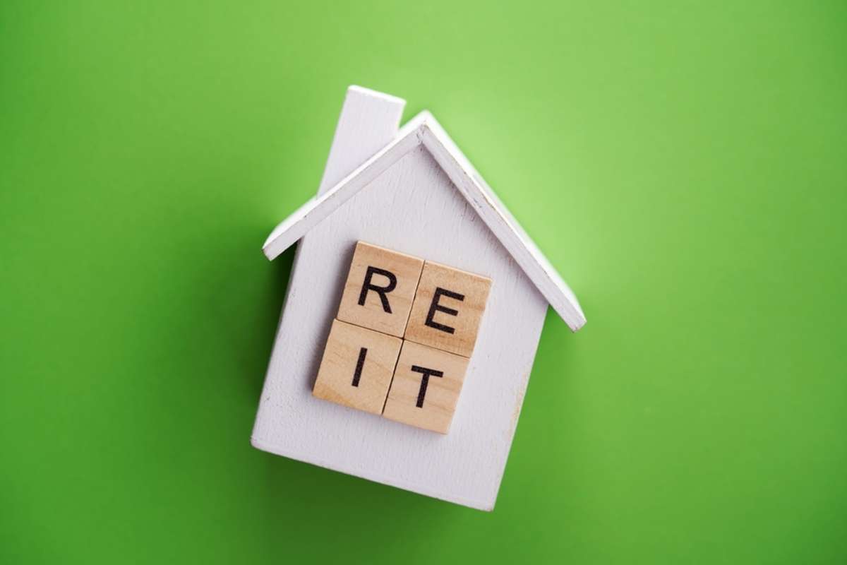 single word reit (real estate investment trust) with mini model house on green color background