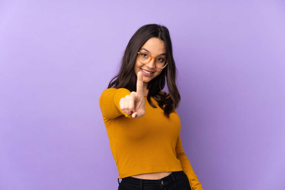 Young mixed race woman isolated on purple background showing and lifting a finger