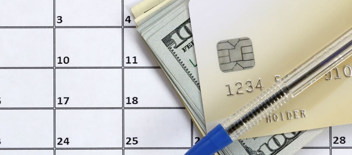 A credit card, cash, and pen on top of a calendar