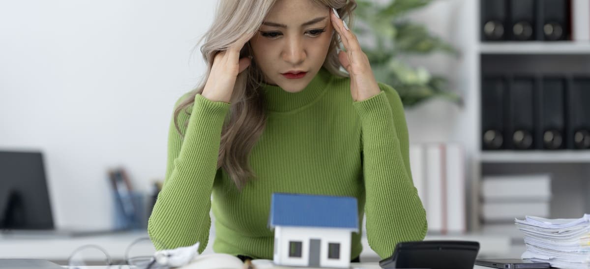 A stressed woman with her hands on her head looking at a small house