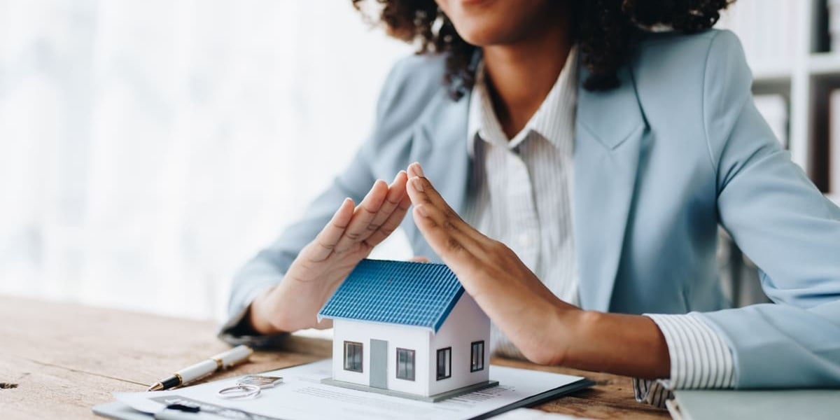 Agent with hands over a tiny house. insurance concept