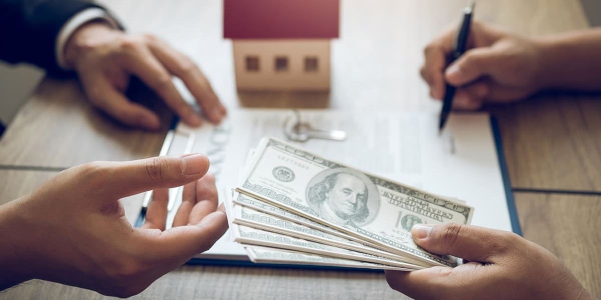 Someone signing a contract and handing money to someone next to a model of a house