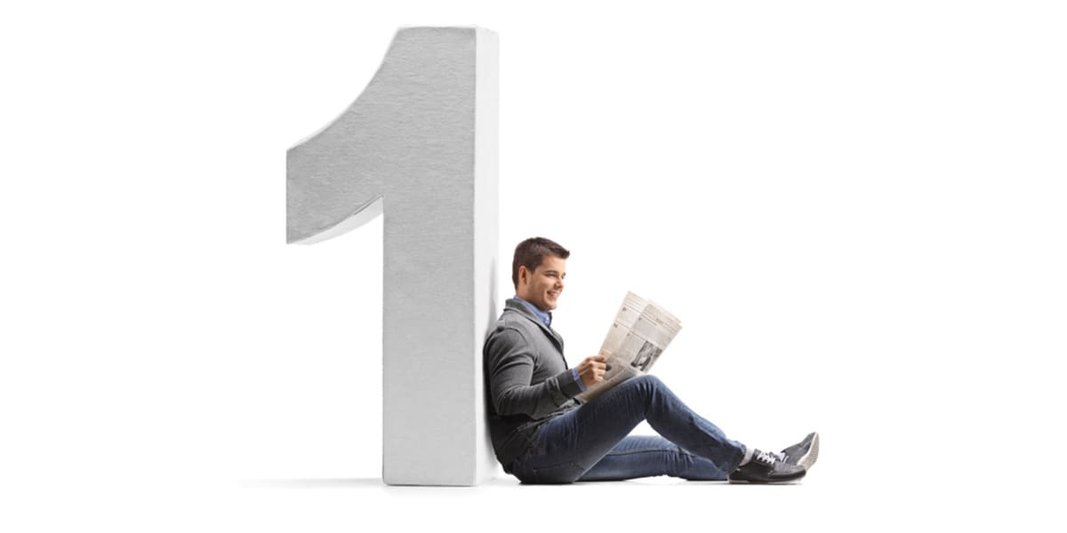 Young man reading a newspaper and leaning against a cardboard number one