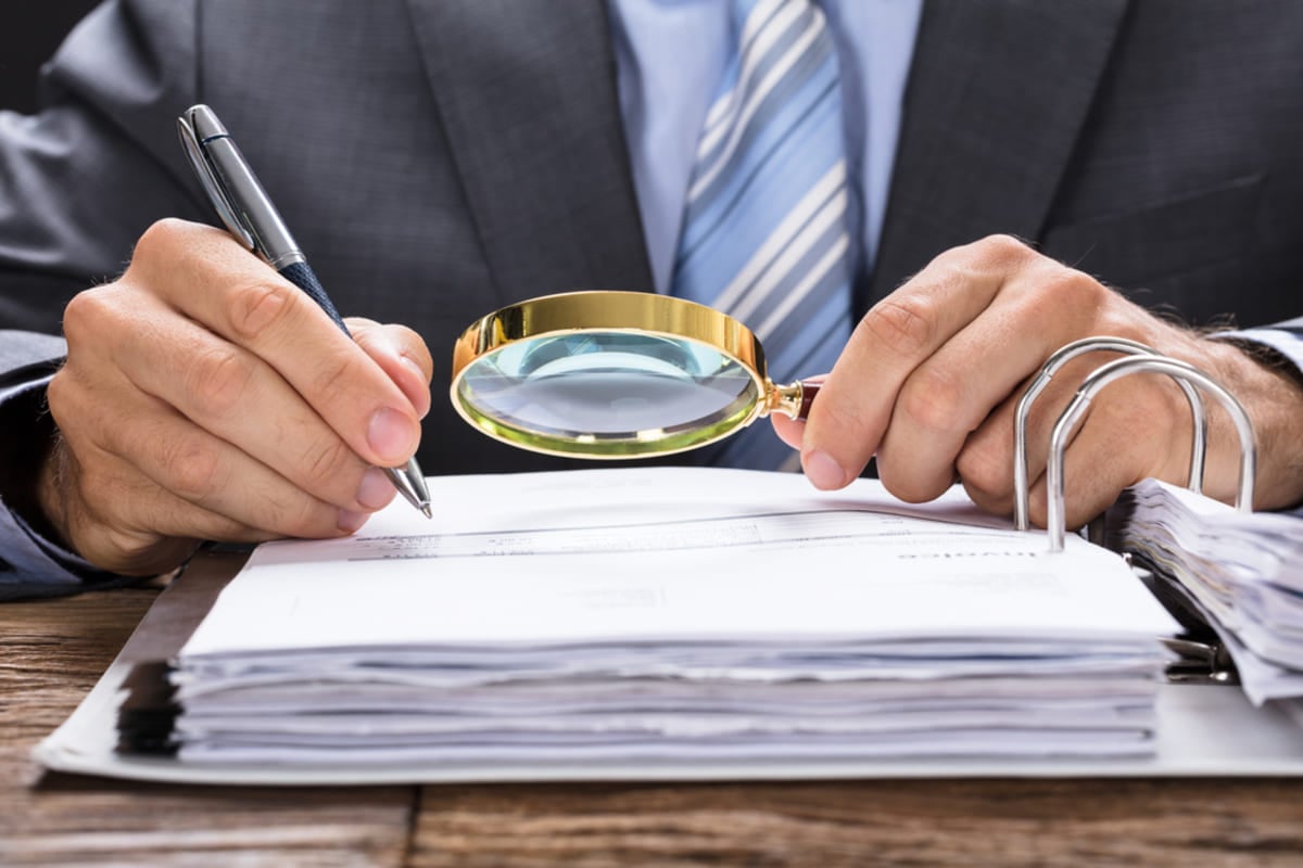 Close-up of hands and a magnifying glass reviewing documents, owner statement concept