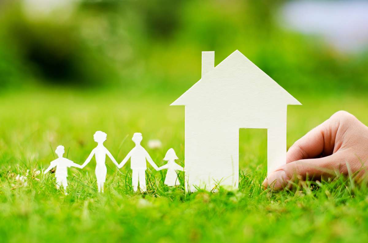 Miniature house with a paper cutout of a family placed on the grass