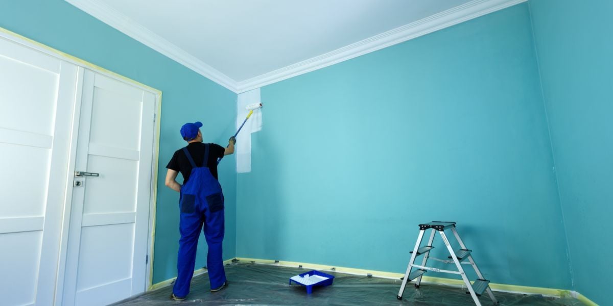 Man in a working overall is painting the wall