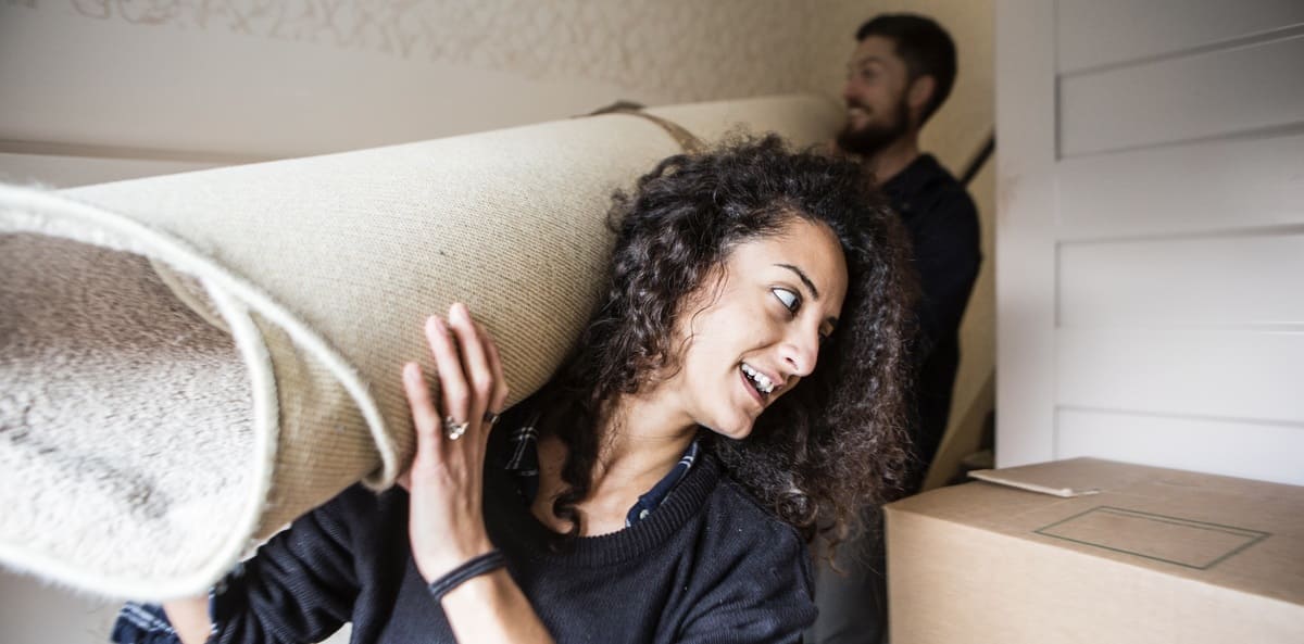 Two people carrying a rug into a new home